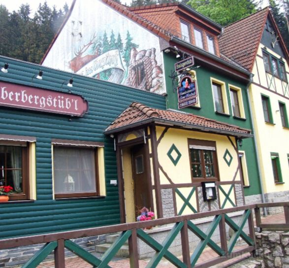 Eingang mit gelbem Fachwerk, grüner Holzfassade und Brücke davor.