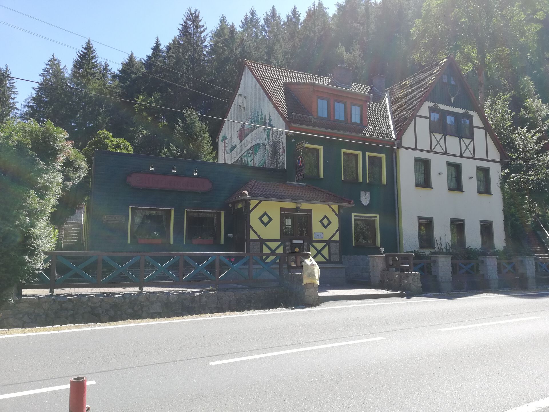 Landhausvilla Zum Kuckuck an der Straße, grün-weißes Fachwerkhaus vor Wald.