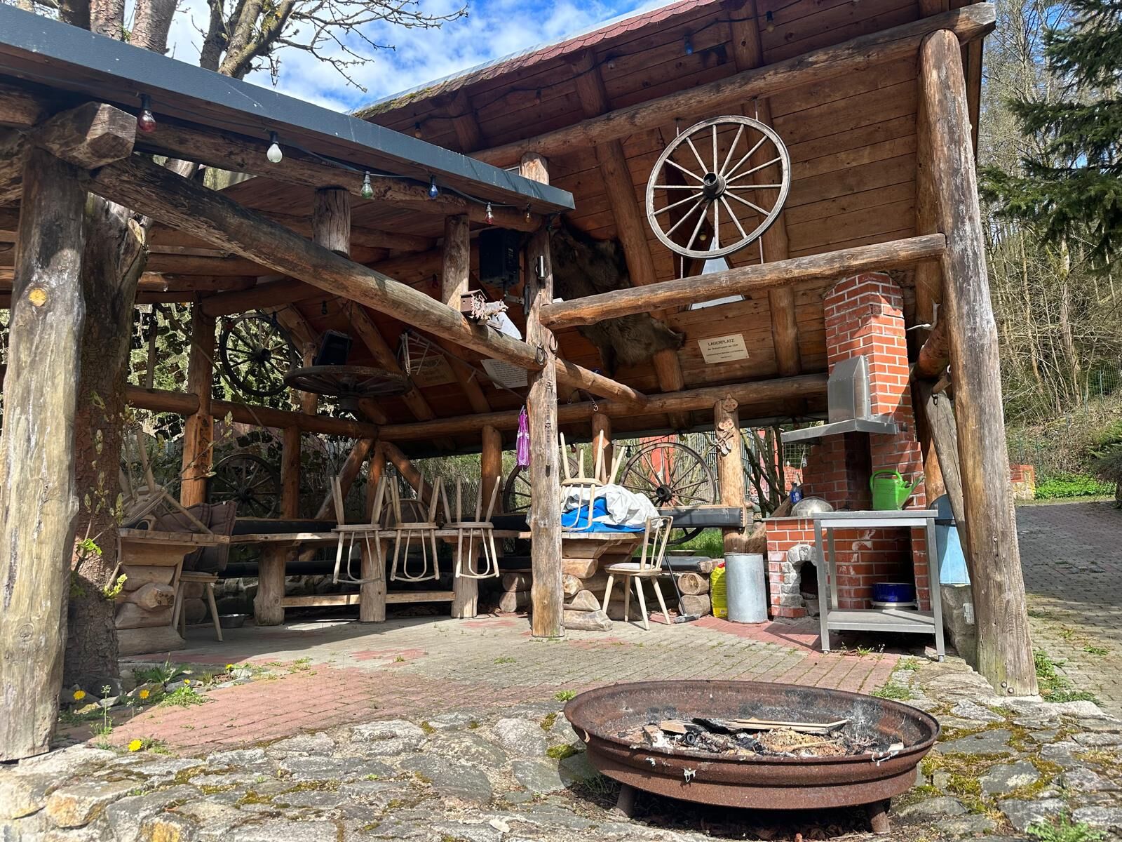 Überdachte Grillstation aus Holz mit Feuerschale davor.