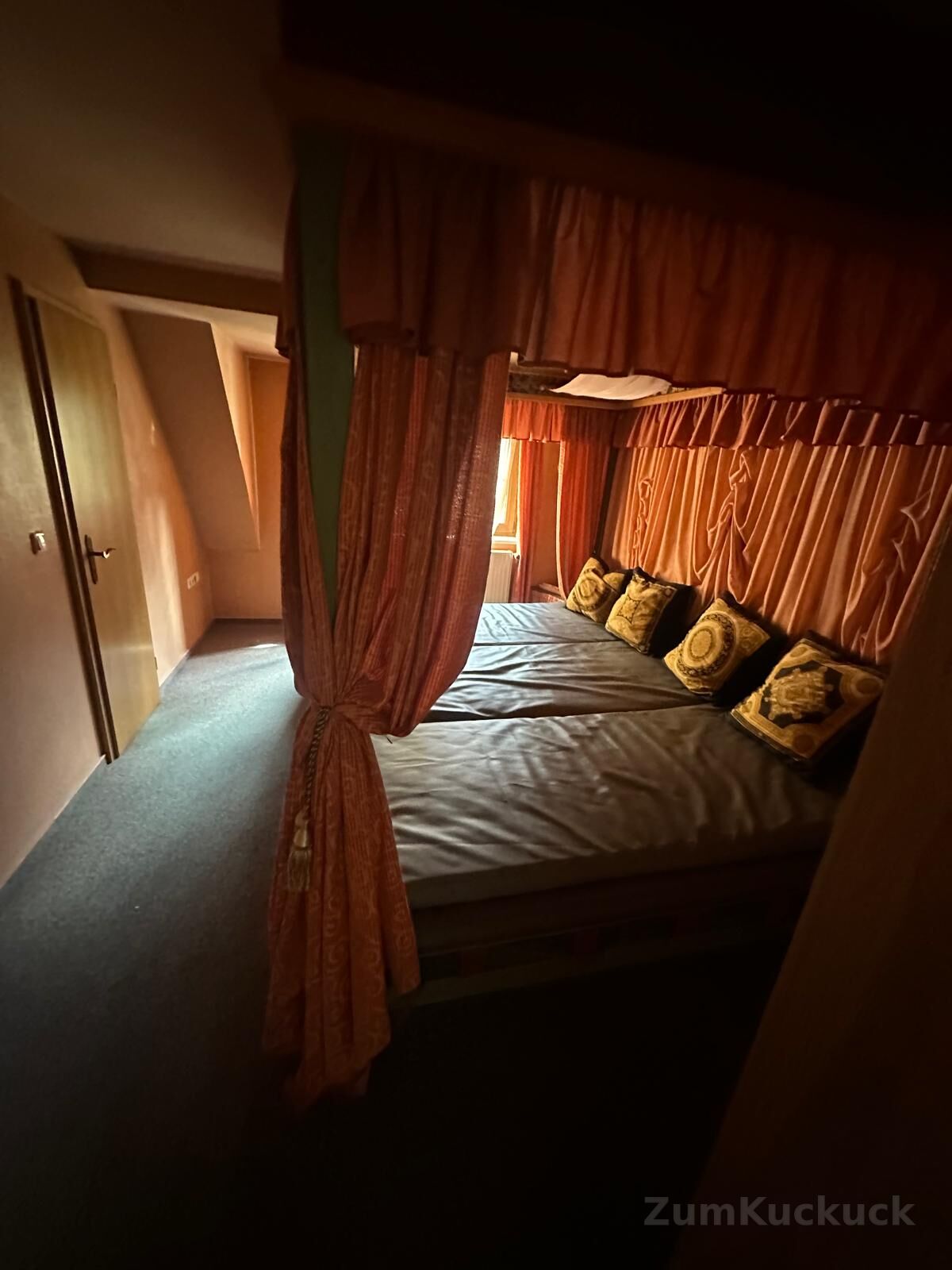 Himmelbett mit orangen Vorhängen und gemusterten Kissen.