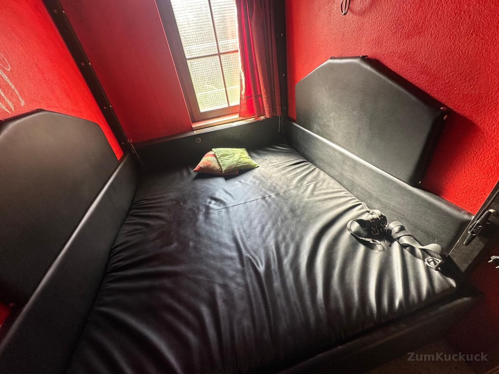 SM-Zimmer mit roten Wänden und schwarzer Liegefläche.