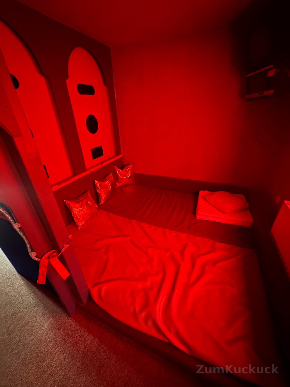 Themenzimmer in rotem Licht mit Liegefläche, Kissen und Wandnischen.