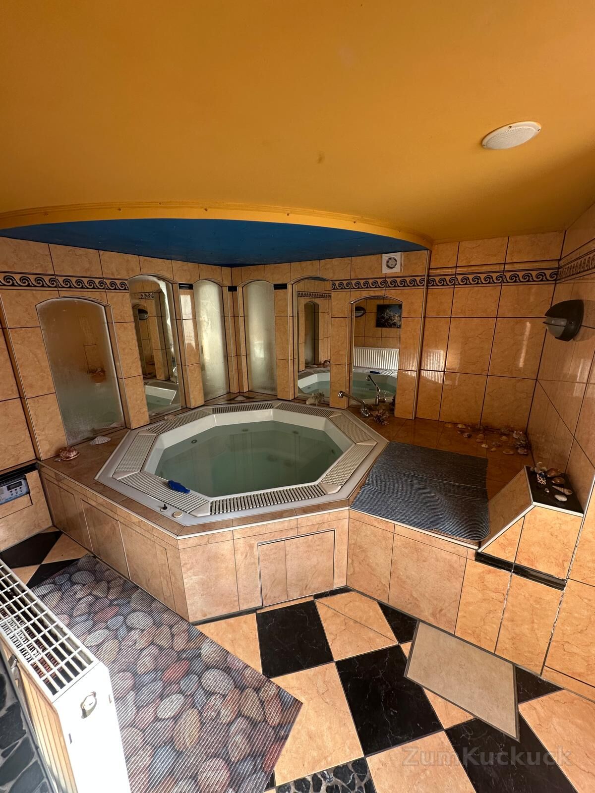 Achteckiger Whirlpool in einem gefliesten Wellnessraum mit Spiegeln.